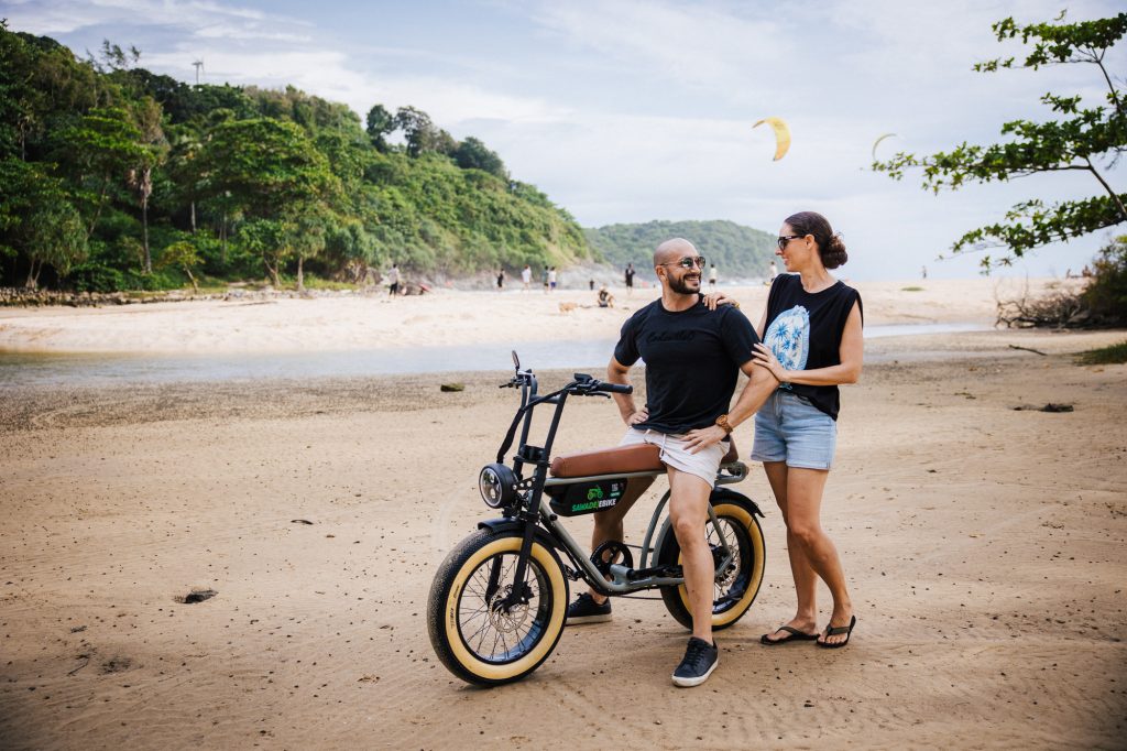 SAWADEEBIKE Vintage Brown electric bike rental Phuket – elegant couple posing by Nai Harn beach seafront on a perfect day